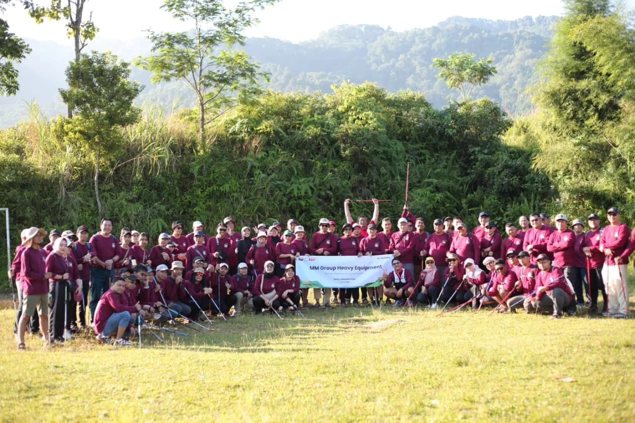 Rombongan karyawan berpose ceria di puncak bukit dengan warna seragam perusahaan.