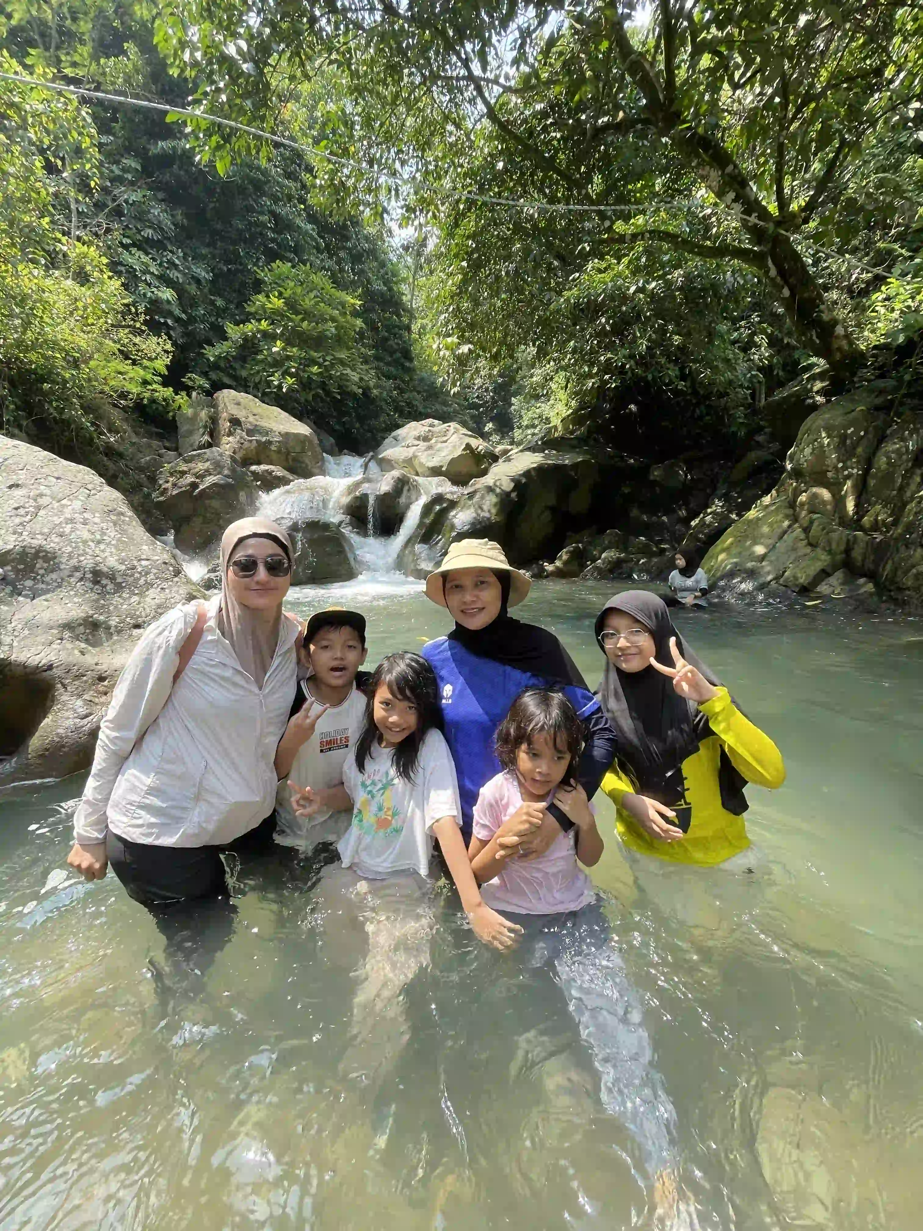 Satu keluarga atau rombongan peserta berpose di sungai yang jernih saat kegiatan trekking.