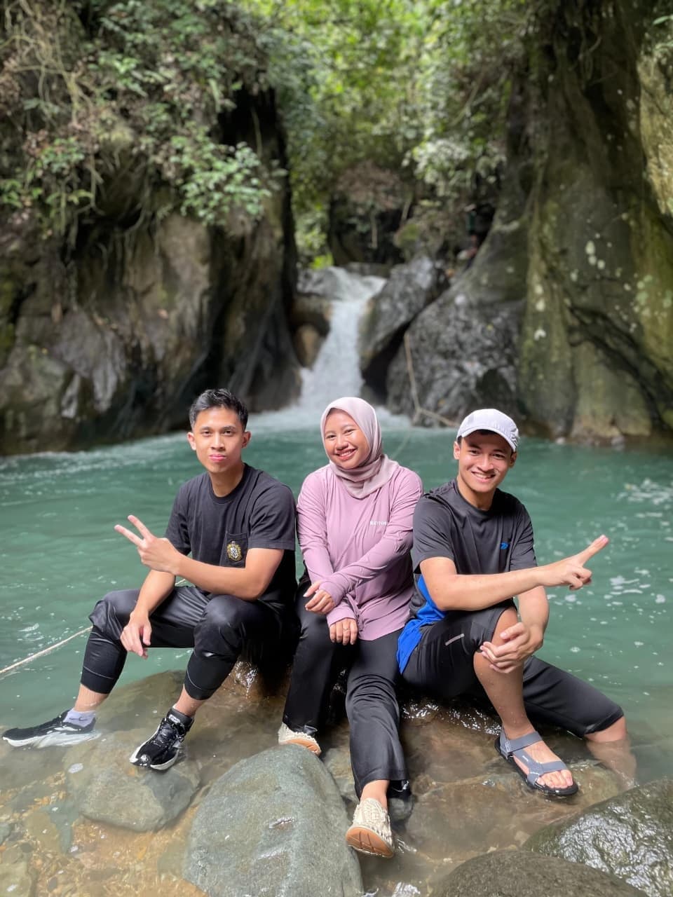 Dua orang peserta menikmati jernihnya air sungai sambil menunjuk ke arah tebing hijau.